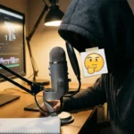 एक क्रिएटर हुडी पहनकर माइक्रोफ़ोन पर रिकॉर्डिंग कर रहा है और अपना चेहरा छिपा रहा है, कंप्यूटर पर वीडियो एडिटिंग चल रही है।